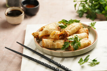 Traditional southeast asian starter dish spring or summer rolls - deep fried dim sum dumplings stuffed with vegetables with soy sauce, fresh coriander on grey plate with black chop sticks, top view