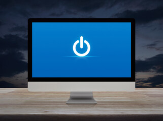 Power button icon on desktop modern computer monitor screen on wooden table over sunset sky,...