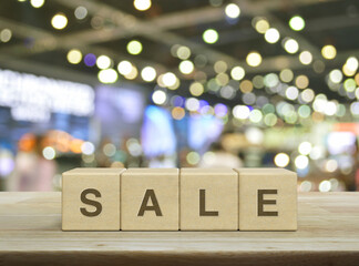 SALE letter on wood block cubes on wooden table over blur light and shadow of shopping mall, Business sales and discounts concept