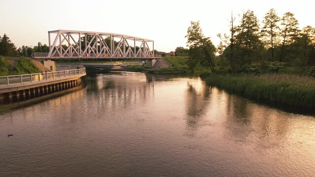 View of the river and railway bridge. Fishing man. Slow drone flight low over the water during sunset. Pisa River, Masuria, Pisz, Poland