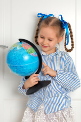 Pretty little European girl kid 6-7 years old holds a world globe in her hand. Distance online learning at home in quarantine. Back to school, learning lessons.