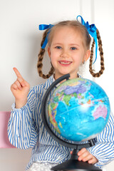 Pretty little European girl kid 6-7 years old holds a world globe in her hand. Distance online learning at home in quarantine. Back to school, learning lessons.