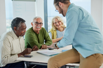 Multicultural group of senior students asking questions their tutor who showing them solution.