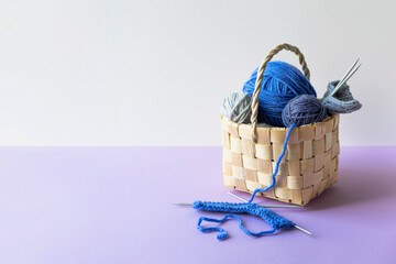 Blue balls of knitting threads on a lilac background in a basket with knitting needles