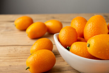 Top view of whole kumquats, in white bowl and on wooden table, horizontal, with copy space