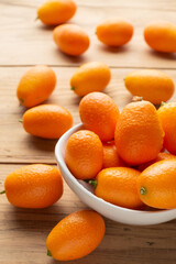 Aerial view of whole kumquats, in white bowl, on wooden table, selective focus, back light, vertical