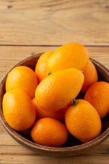 Top view of whole kumquats, in wooden bowl, on wooden table, selective focus, vertical