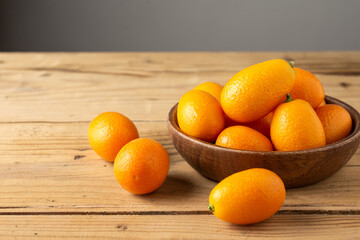 Top view of orange kumquats, in wooden bowl, on wooden table, selective focus, horizontal, with copy space
