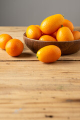 Top view of orange kumquats, in wooden bowl, on wooden table, selective focus, gray background, vertical, with copy space