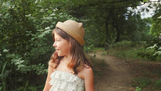 Summertime. Little girl in a straw hat and dress walking in the park. Slow motion. Follow shot. The concept of childhood and Children's Day.
