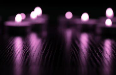 A group of tea candles blurred highlighted by strong purple  lighting reflecting  background.