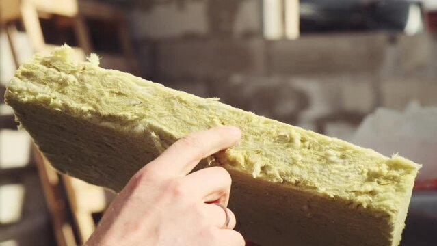 A man shows a mineral wool with his finger. Mineral wool in a section. Material for warming the walls of the house. Slow motion
