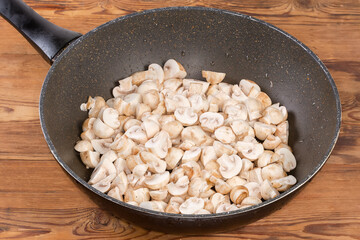 Sliced raw button mushrooms in frying pan on rustic table