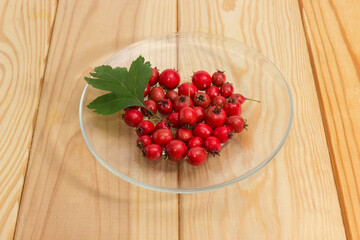 Hawthorn fruits on glass saucer with leaf on rustic table