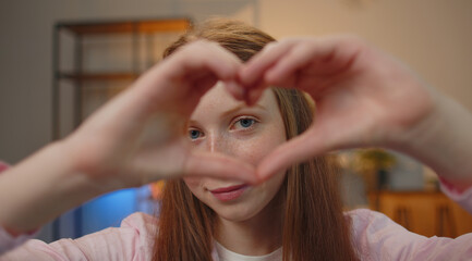 Fototapeta premium I love you. Teen child girl makes symbol of love, showing heart sign to camera, express romantic feelings, express sincere positive feelings. Charity, gratitude, donation. Children close-up happy face