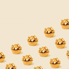Creative pattern made of golden baking cups with cubes on pastel beige background. Copy space. Abstract food composition.