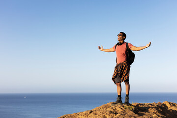 Young man standing on the stone with raised up arms. Tourist man on the top of the mountain.