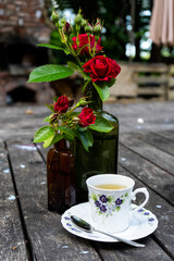 A white cup of tea on a wooden table with red roses.  a red rose and one white cup on a wooden table. Selective focus.