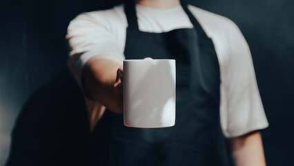 Barista wearing apron showing cup of coffee mockup.
