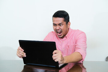 Adult Asian man grabbing his laptop screen with engry expression