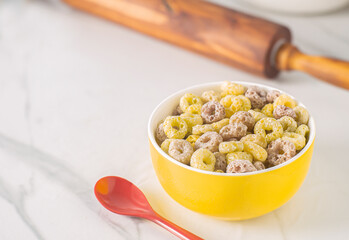 An image close-up and selacted focus many colors such as yellow and pink cereal in the bowl on the table with a red spoon and which is a breakfast food fresh with copy space for text.