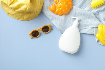 Sunscreen bottle with sunglasses, sand molds, towel, panama hat on blue table. Summer vacation, kids sun protection concept.