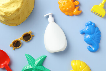 Baby sun protection cream pump bottle with sand molds, sun glasses, panama hat on blue table. Flat lay, top view.