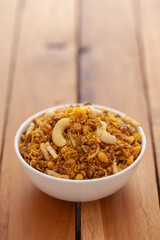 Close-Up of Dal Biji or Dal moth, made with roasted Masoor Dal (black lentils) and small besan sev, garnished with fried cashew nuts  in white ceramic bowl over wooden  background