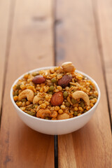 Close-up of Shahi Mixture made from almonds, cashew, corn flakes, peanut, Indian spicy snacks (Namkeen), in white ceramic bowl over wooden  background