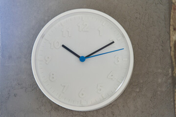 White big wall clock with blue second hand on rough cement wall. High quality photo