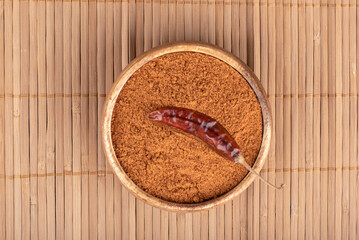 Hot pepper pod in a bowl with ground red pepper on a food mat.