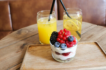 summer desserts with berries in a glass bowl and large glasses of homemade lemonade on a wooden  in a cafe