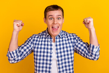 Happy winner. Young handsome man gesturing fist up while standing against yellow vivid background...