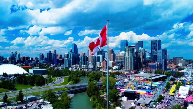 Calgary Stampede arial drone hold horizon city skyline sunny summer day largest Canada flag in the foreground MNP community sports Repsol Centre divided by river running lush green thousands of people