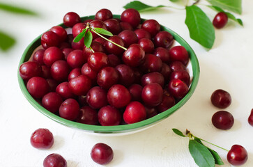 Many ripe red cherries in a white ceramic bowl with a green stripe on a light background. Harvesting concept. Horizontal orientation. Top view