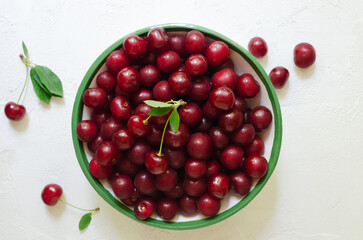 Many ripe red cherries in a white ceramic bowl with a green stripe on a light background. Harvesting concept. Horizontal orientation. Top view