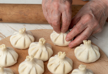cook making khinkali, dumplings, meat in the dough cooking with hands. Juicy meat in a dough with spicy herbs to dab in hands. Tasty hot Georgian, Eastern, Buryat dish.