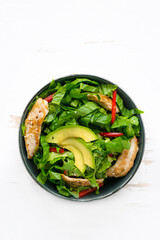 Healthy  vegetable buddha bowl salad with fried chicken and avocado, peppers and leaf lettuce on a white plate.