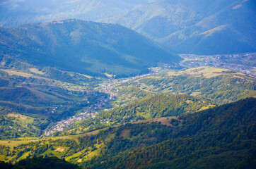 mountain landscape on a sunny autumn morning. village in the distant valley. view from the top of a forested hill