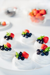 Meringue dessert Pavlova cake with fresh cream, strawberries and blueberries, decorated with mint on the white plate. Recipes for delicious light desserts. Confectionery cafe menu. Selective focus