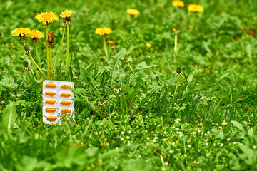 White blister with orange red pills on a green lawn with dandelions