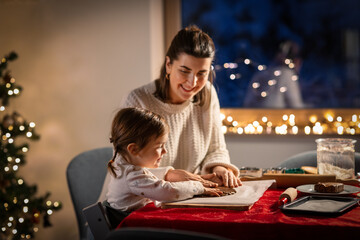 family, cooking and winter holidays concept - happy mother and baby daughter having fun with dough for gingerbread cookies at home on christmas