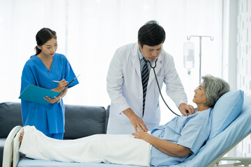 Obraz premium Doctor and patient in the patient room at hospital. Male doctor using stethoscope examining old woman patient’s heartbeat. Male doctor visiting and checking female patient. Health care concept