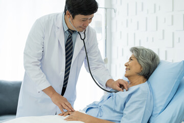 Obraz premium Doctor and patient in the patient room at hospital. Male doctor using stethoscope examining elderly woman patient’s heartbeat. Male doctor visiting and checking female patient. Health care concept