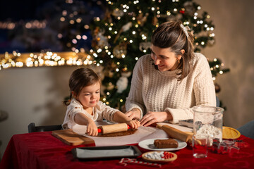 family, cooking and winter holidays concept - happy mother and baby daughter with rolling pin making gingerbread cookies from dough at home on christmas