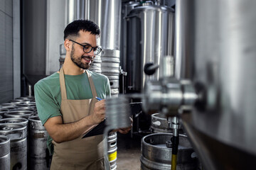 Man working in craft brewery examining production of the beer.