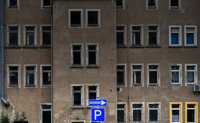 Old ugly apartment block with dark windows and the signs for a one-way street and a parking lot,...