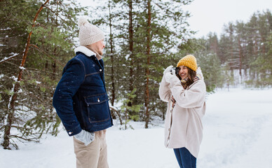 Fototapeta na wymiar people, love and leisure concept - happy smiling woman photographing man in winter forest