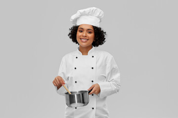 culinary and people concept - happy smiling female chef in toque with saucepan cooking food over grey background