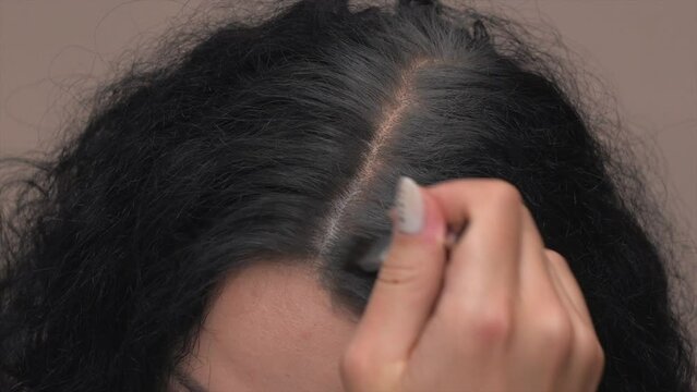 Hair coloring close-up. Hairdresser paints brunette hair roots with brush. 